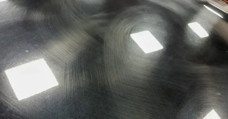 Close-up of swirl marks on black car paint surface under detailing light